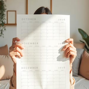 2026 calendar printable showing three consecutive months on a vertical sheet with minimalist thin grey lines and typography, held in a hand against a simple neutral background surface.