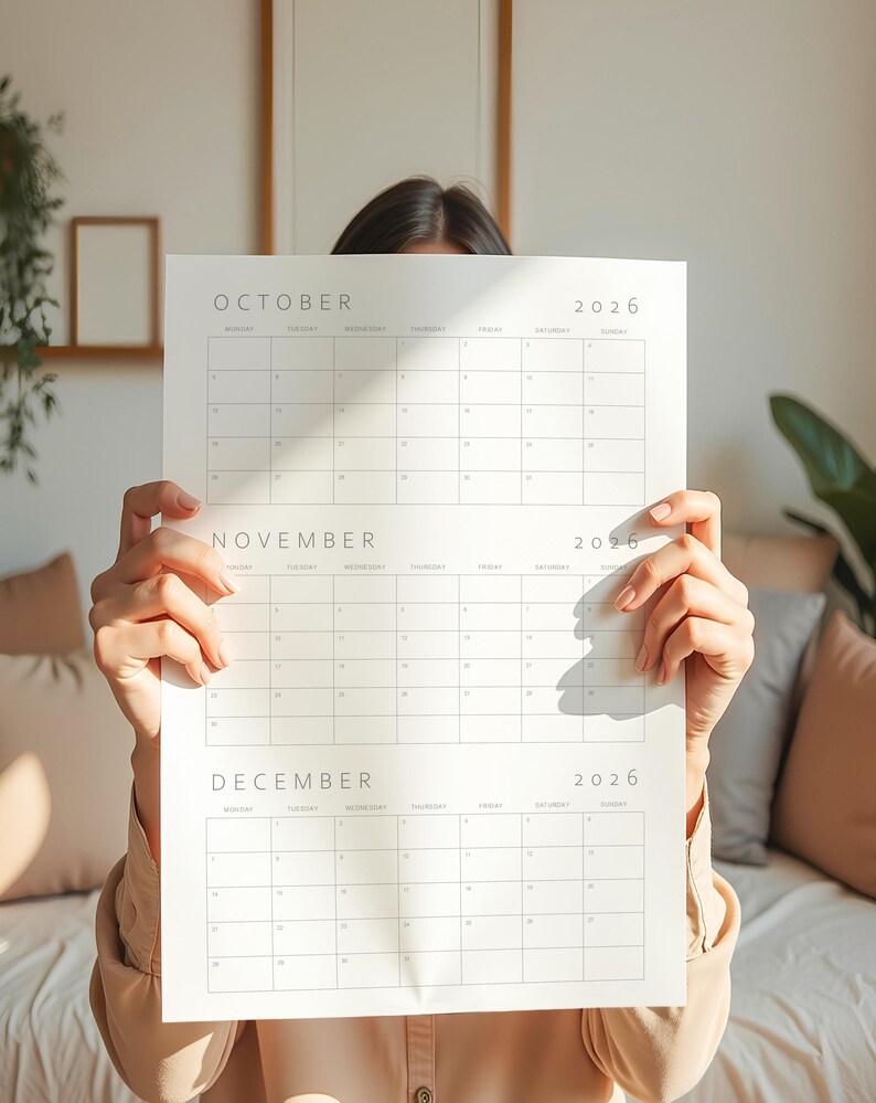 2026 calendar printable showing three consecutive months on a vertical sheet with minimalist thin grey lines and typography, held in a hand against a simple neutral background surface.