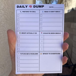 May include: A white notepad with the words "DAILY DUMP" at the top, featuring checkboxes and sections for tasks like "Pretend to Call" and "Might Actually Do." The notepad is held in a hand.