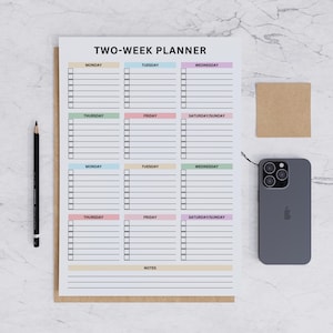 Könnte beinhalten: Ein Zwei-Wochen-Planer mit farbcodierten Wochentagen, einschließlich Montag bis Sonntag. Der Planer hat Platz für Notizen und eine Checkliste für jeden Tag. Ein Bleistift, ein graues Smartphone und ein kleiner quadratischer Haftzettel sind ebenfalls vorhanden.