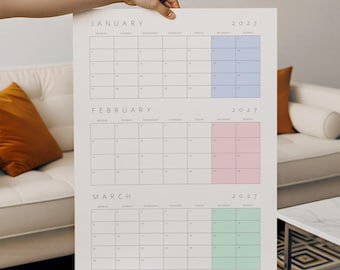 May include: A 2027 wall calendar featuring the months of January, February, and March. Each month is displayed in a grid format with black text on a white background. January has light blue weekend columns, February has pink, and March has green.