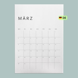 Kalender 2026 deutschsprachig, minimalistisches Design mit Monatsübersicht, auf weißem A4-Blatt gedruckt, liegt auf heller Holzoberfläche, natürliche Lichtverhältnisse.