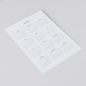 One-page 2026 calendar PDF printout in minimalist grey font, shown on A4 white paper resting on a neutral concrete surface, with soft shadows and a clean background.