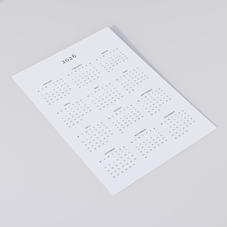 One-page 2026 calendar PDF printout in minimalist grey font, shown on A4 white paper resting on a neutral concrete surface, with soft shadows and a clean background.