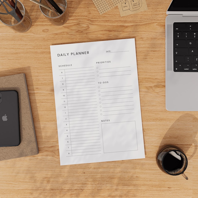 The planner template printed on Letter paper, flat on white desk with black pen and notebook nearby, showing boxes for to-dos, notes, and schedule from morning to evening.
