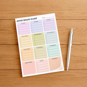 A 4x6 inch ADHD brain dump sticky note pad on a desk, showing a structured layout with labeled sections and checkboxes for thoughts, tasks, ideas, notes, and reminders printed on white paper.