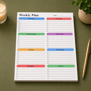 Weekly desk planning notepad with spacious checklist layout and soft pastel weekday headers shown on clean beige surface, featuring large writing sections and organized planner format.