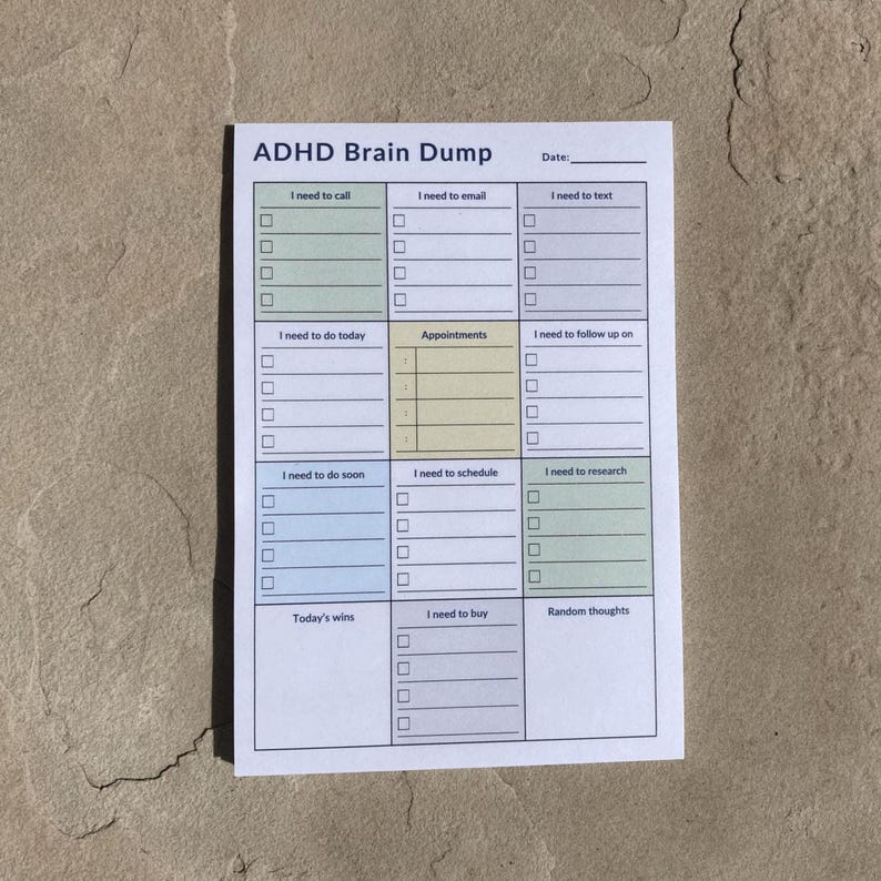 ADHD daily planner sticky note pad with colorful section headers lies flat on a textured stone surface in an outdoor setting, showing tasks, schedule, calls, and brain dump layout.