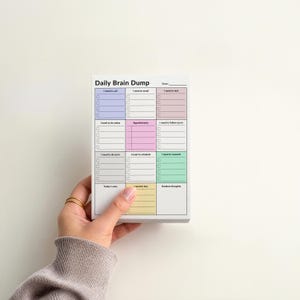 Hand holding a 4x6 ADHD sticky notes planner pad with shaded sections for tasks, calls, appointments, and brain dump, compact size with color-coded layout for focus and daily organization.