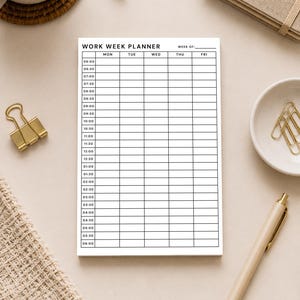 May include: A white Work Week Planner with a grid layout for scheduling appointments, with the days of the week across the top. The planner is surrounded by a pen, a cup of coffee, a notepad, and other office supplies.