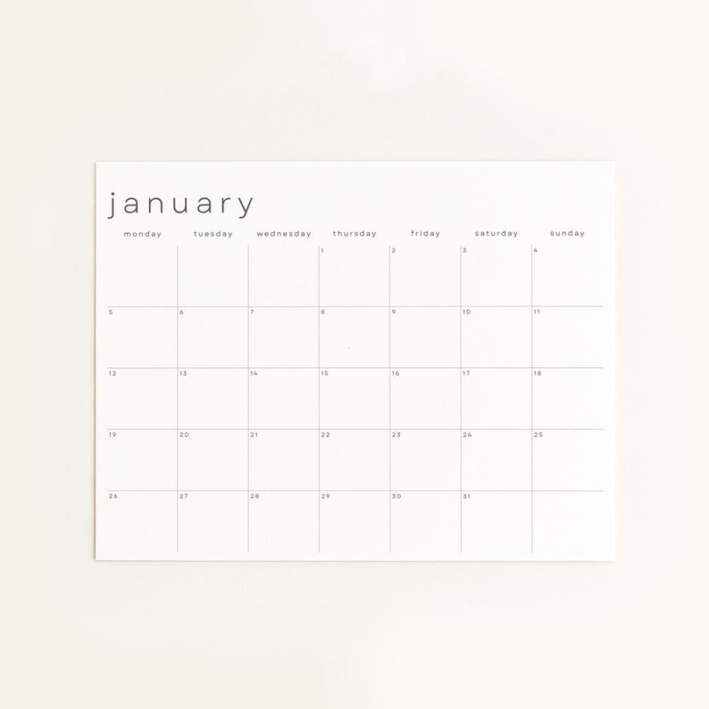 Overhead photo of May 2026 planner page resting on a wooden surface. The landscape monthly grid has slim gray dividers, small weekday labels, and black date numbers on bright paper.