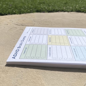 Compact daily brain dump notepad displayed on a large rock outdoors, featuring bold printed labels for planning tasks, appointments, and reminders in a structured format.