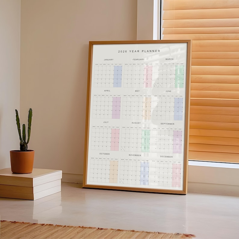 A close-up of a full year 2026 planner printed on matte 200 gsm paper, featuring a minimalist layout with vibrant pastel accents for weekends and a simple black and white grid design.