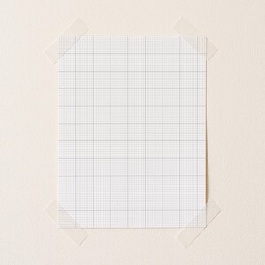 A4 printable grid paper with small ten-per-inch squares, printed on matte white paper, positioned diagonally on a clean desk surface with even line visibility.