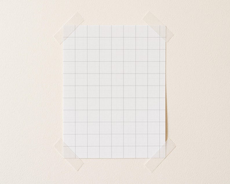 A4 printable grid paper with small ten-per-inch squares, printed on matte white paper, positioned diagonally on a clean desk surface with even line visibility.