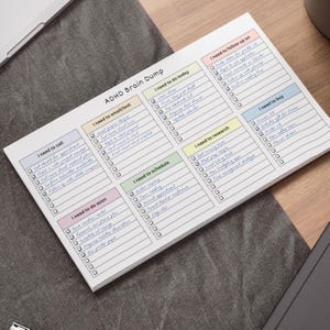White pastel ADHD brain dump sticky note pad showing eight checklist headings with checkboxes on a single printed sheet in portrait orientation, held in a hand against a blurred background.