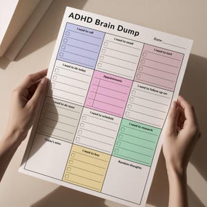 A person holding a printed ADHD brain dump planner, showing sections for tasks, phone calls, and notes. The planner is in portrait orientation and placed against a neutral, soft background for clarity.