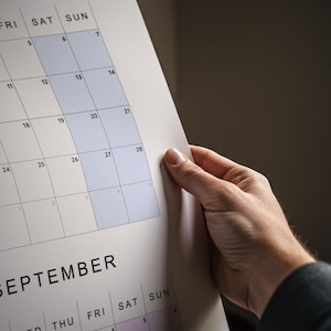 White sheet showing a 2026 year-at-a-glance wall calendar, vertical layout with pastel color blocks, all months displayed in a single grid, printed on thick paper.