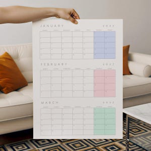 May include: A 2027 wall calendar featuring the months of January, February, and March. Each month is displayed in a grid format with black text on a white background. January has light blue weekend columns, February has pink, and March has green.