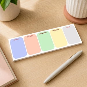 May include: A rectangular weekly planner notepad featuring five rounded-corner sections in light blue, peach, light green, yellow, and light grey. Each section is labelled with the days of the week: Monday, Tuesday, Wednesday, Thursday, and Friday.