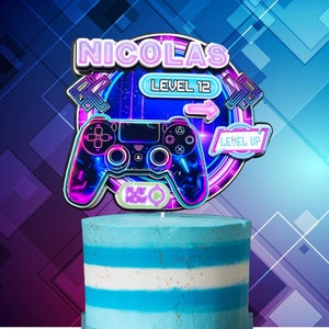 Peut inclure: Un topper de gâteau de manette de jeu vidéo rose et bleu néon avec le nom "NICOLAS" et le texte "Niveau 12" et "Niveau supérieur".