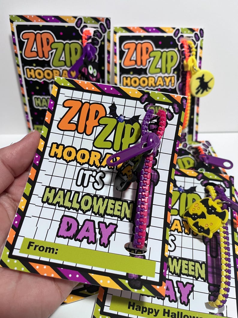 Puede incluir: Una tarjeta con tem&aacute;tica de Halloween con un brazalete de cremallera morado y rosa adjunto. La tarjeta tiene un fondo verde y amarillo con el texto "ZIPZIP HOORAY! IT'S HALLOWEEN DAY" y un espacio para "From:".