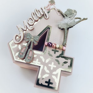 May include: A pink number four cake topper with a gold glitter ballerina, a pink bow with a pearl, and the name "Molly" in pink letters.