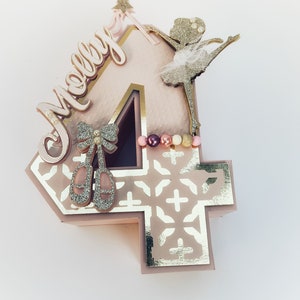 May include: A pink and gold number four cake topper with a ballerina silhouette, a star wand, and the name "Molly" in gold script.
