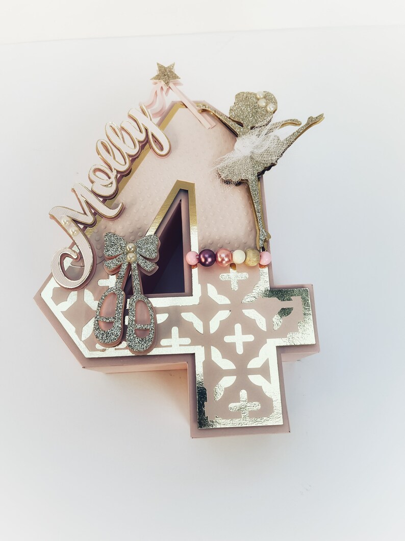 May include: A pink and gold number four cake topper with a ballerina silhouette, a star wand, and the name "Molly" in gold script.