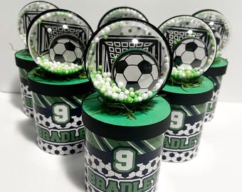 May include: Six small green, black, and white favor boxes with a soccer ball and goal design. Each box has the name "Bradley" and the number "9" printed on it.