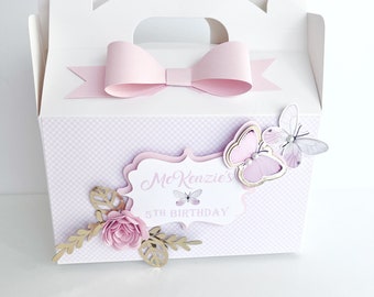 May include: A white favor box with a pink bow and a pink and gold butterfly design. The box has a gingham pattern and says "McKenzie's 5th Birthday".