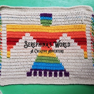 Puede incluir: Manta de crochet color crema con un diseño Thunderbird colorido en tonos arcoíris. La manta tiene bordes con flecos con hilo de arcoíris y el texto "Serephina's World A Creative Adventure".