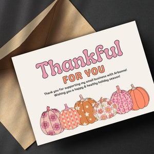 May include: A white card with the text "Thankful for you" in pink and orange letters. The card has a fall theme with five pumpkins with different patterns in pink, orange, and white.