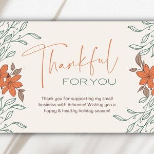 May include: A beige card with a handwritten message that says "Thankful for you". The card is decorated with green leaves and orange flowers.