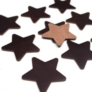 May include: A collection of dark brown leather star shapes scattered on a white surface. One star is a lighter tan color. The stars vary in size and are cut from leather.