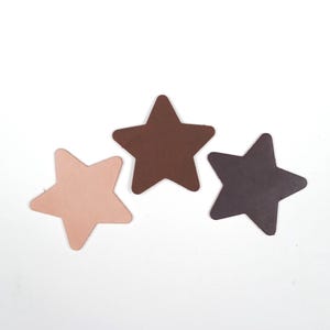 Può includere: Tre stelle di cuoio in varie tonalità di marrone e rosa su sfondo bianco. Le stelle sono tagliate da un materiale liscio e hanno un semplice design a cinque punte. I colori includono un rosa chiaro, un marrone medio e un marrone scuro.