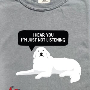 K&ouml;nnte beinhalten: Ein graues T-Shirt mit einer Illustration eines wei&szlig;en Pyren&auml;enberghundes und einer Sprechblase mit dem Text "Ich h&ouml;re dich, ich h&ouml;re einfach nicht zu".