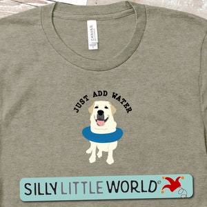 K&ouml;nnte beinhalten: Ein khakifarbenes T-Shirt mit einem wei&szlig;en Labrador Retriever, der eine blaue Schwimmweste tr&auml;gt. Der Text "Just Add Water" befindet sich &uuml;ber dem Hund. Der Text "Silly Little World" befindet sich am unteren Rand des T-Shirts.