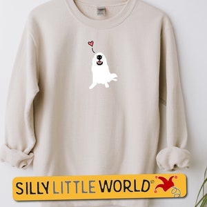 May include: A cream-coloured sweatshirt with a white cartoon dog wearing a red heart above its head. The text "SILLY LITTLE WORLD" is printed on a yellow banner with a red jester hat.