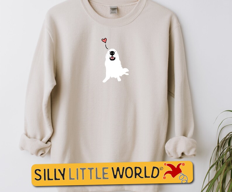 May include: A cream-coloured sweatshirt with a white cartoon dog wearing a red heart above its head. The text "SILLY LITTLE WORLD" is printed on a yellow banner with a red jester hat.