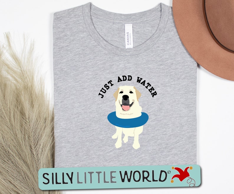 K&ouml;nnte beinhalten: Ein graues T-Shirt mit dem Text "Just Add Water" und einem Cartoon-Bild eines gelben Labradors, der eine blaue Schwimmweste tr&auml;gt. Der Text "Silly Little World" befindet sich am unteren Rand des Shirts.