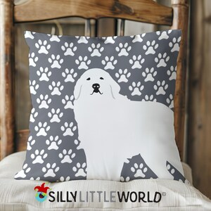 May include: A gray throw pillow with a white paw print pattern and a white silhouette of a Great Pyrenees dog. The pillow features the text "Silly Little World".