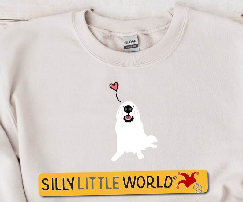 May include: A white sweatshirt featuring a cartoon illustration of a white dog with a red heart above its head. The text "SILLY LITTLE WORLD" is printed in yellow on a black rectangle at the bottom of the image.