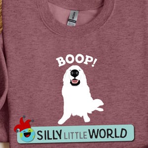 May include: A maroon sweatshirt with a white graphic of a smiling Great Pyrenees dog with the text "BOOP!" and the text "SILLY LITTLE WORLD" below the dog.