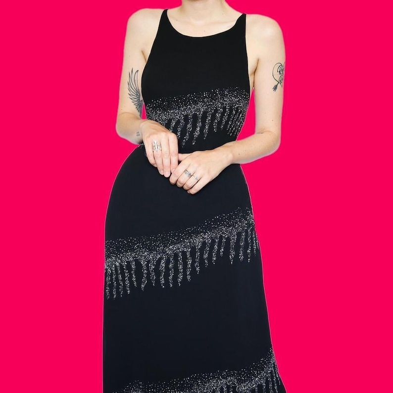 May include: A black sequined dress with a fringe hem. The dress has a sleeveless design and a scoop neckline.