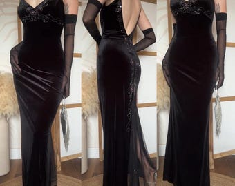 May include: A floor-length black velvet gown featuring thin spaghetti straps, a V-neckline, and intricate beadwork on the bodice. The dress includes a low-cut back, a sheer mesh panel at the hem, and is paired with matching sheer black opera gloves.