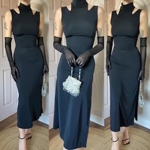 May include: A black sleeveless dress with a high neck and a fitted silhouette. The dress has a small slit in the front and is paired with sheer black gloves and a silver beaded clutch.