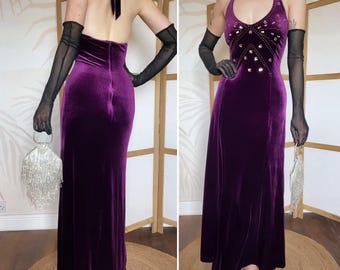 May include: A floor-length deep purple velvet halter dress featuring a V-neckline adorned with scattered silver rhinestones. The garment is paired with sheer black elbow-length gloves and a silver metallic fringe handbag with a circular handle.