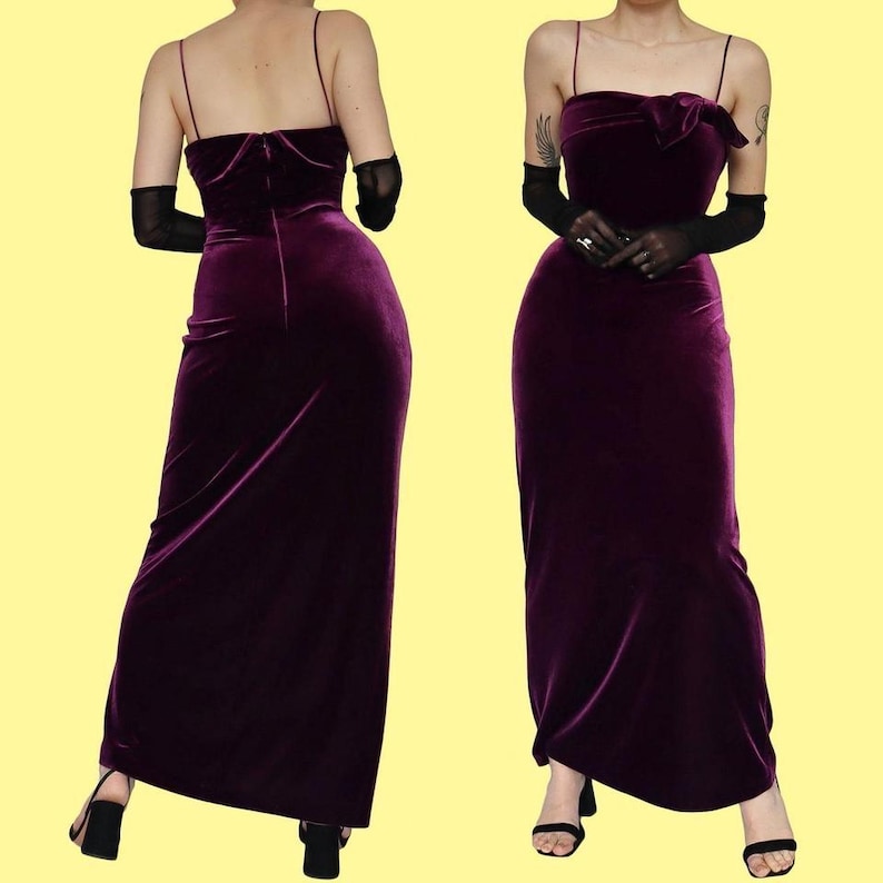 May include: A deep purple velvet gown with spaghetti straps and a fitted bodice. The dress has a floor-length skirt and is shown from the front and back. The model is wearing black gloves and heels. The dress features a bow detail at the bust.