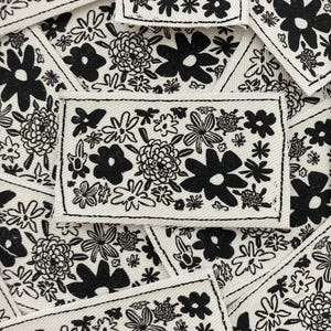 Puede incluir: Una colección de parches de tela blanca con diseños florales negros. Los parches presentan varias flores y hojas estilizadas, creando una estética caprichosa y moderna.